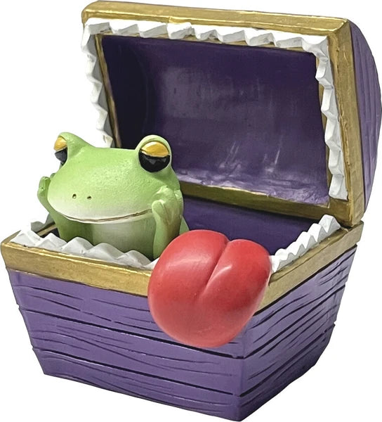 Green frog figurine inside a purple treasure chest with pointy teeth around the opening and a tongue sticking out on a white background